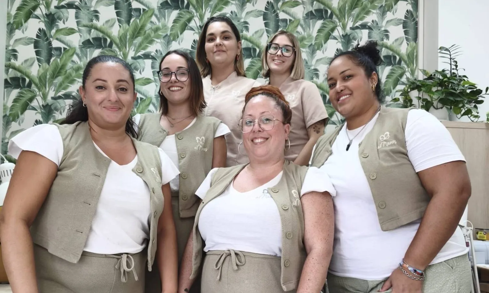 El equipo de aManos sonriendo frente al papel pintado tropical